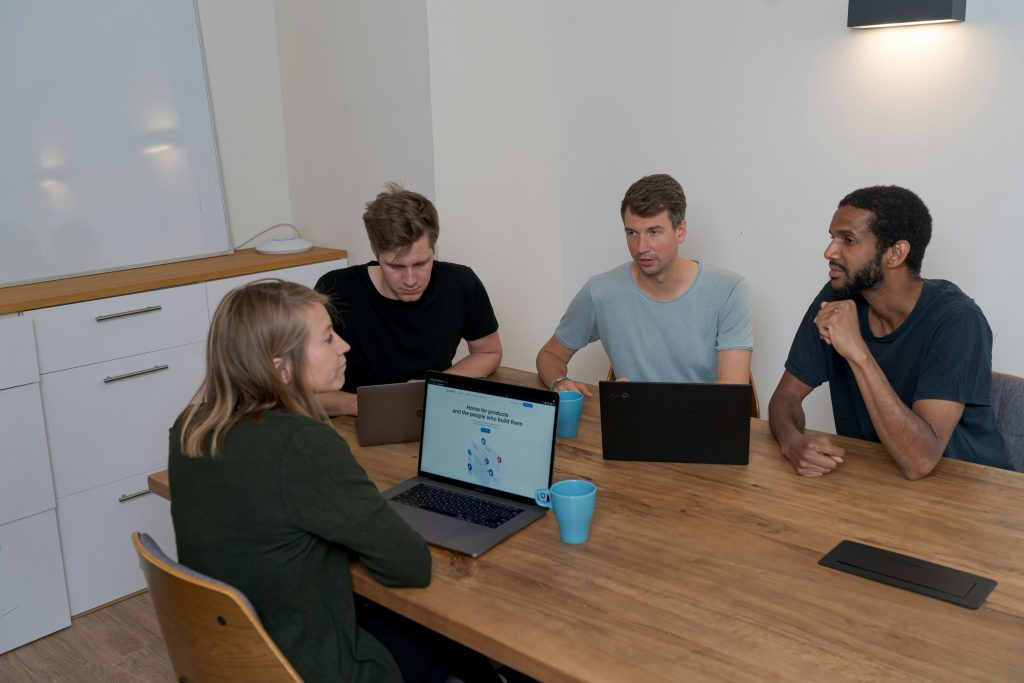 A diverse team of startup founders collaborating around a wooden table in a bright, modern office, reviewing business data and legal documentation on laptops.